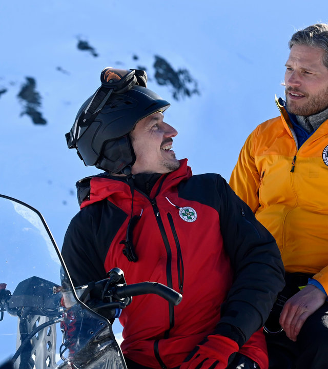 "Die Bergretter: Giftiges Erbe": Vor einer Schneekulisse sitzt Tobi (Markus Brandl) auf einem Ski-doo und blickt lachend über die Schulter nach hinten zu Markus (Sebastian Ströbel).