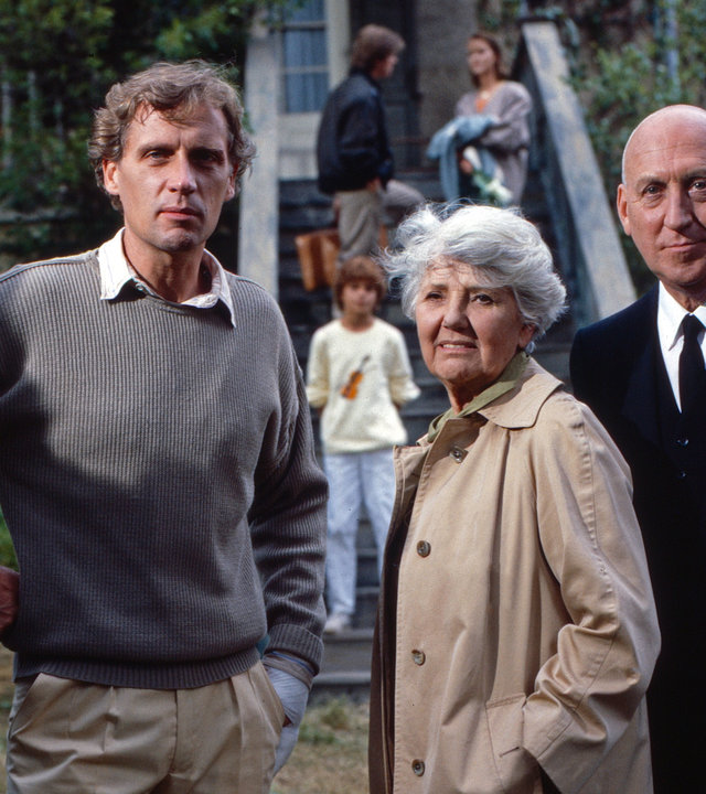 "Oliver Maass - Das Spiel mit der Zaubergeige": Michael Maass (Robert Atzorn), Louise Maass (Jane Tilden) und Eickelberg (Karl Lieffen) stehen nebeneinander in einem Vorgarten und schauen ernst in die Ferne.