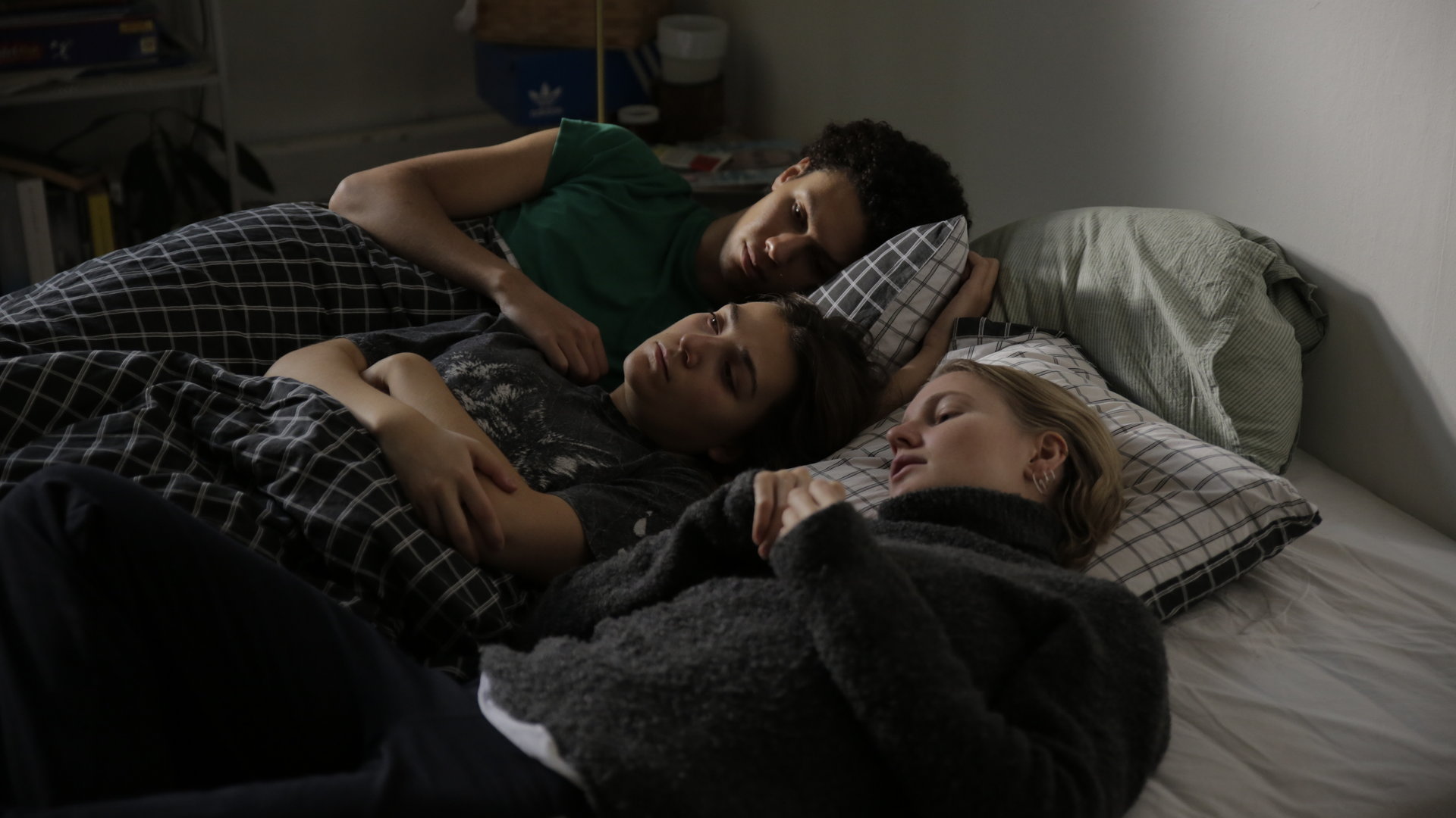 "About Saturday - Keine Angst mehr": Klara (Darin Hagi), Lotte (Hanna Heider Hov) und Mo (Kayd Wacays) liegen zusammen auf einem Bett. Dabei spenden Mo und Lotte Klara Trost indem sie ihre Hände auf Klaras Schultern legen.