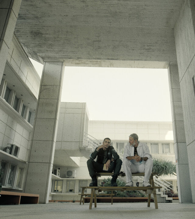 "Borders - Krieg": Avi (Ben Sultan) und Chicko (Haim Zanati) sitzen auf einem Krankenhausflur nebeneinander auf einem Tisch und unterhalten sich. Avi raucht eine Zigarette.