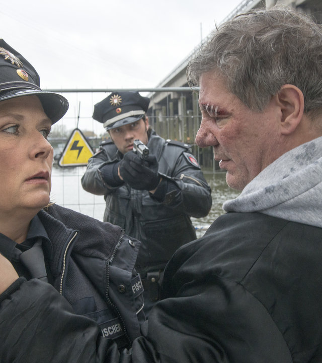 "Notruf Hafenkante - Lucky Punch": Mitschke (Claude-Oliver Rudolph) packt Claudia (Janette Rauch) am Kragen und wirkt sehr aggressiv. Im Hintergrund steht Mattes (Matthias Schloo) mit gezogener Waffe.