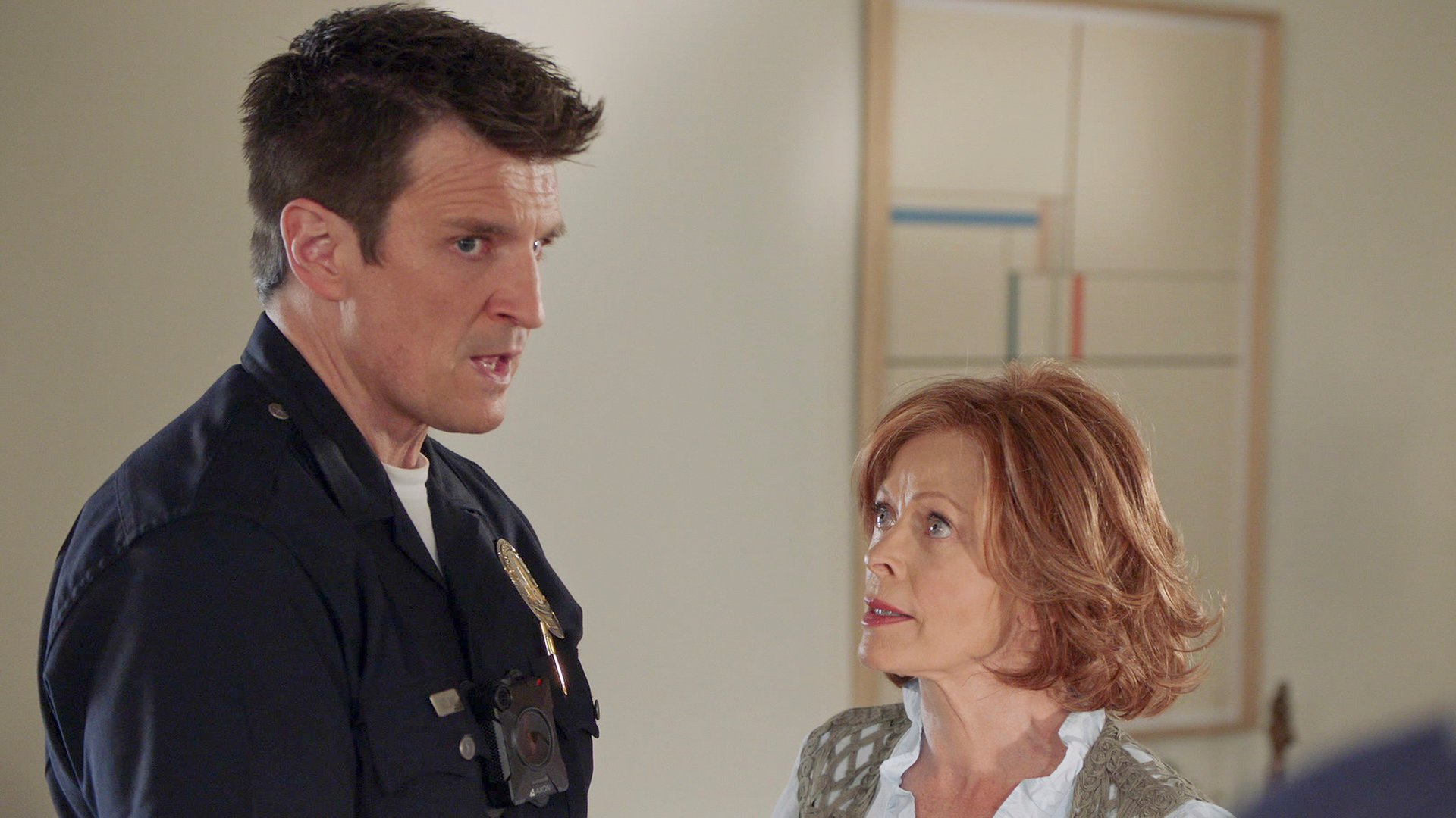 "The Rookie - Familienbande": Nolan (Nathan Fillion) steht Evelyn (Frances Fisher) in einem Gang gegenüber und schaut abgelenkt zur Seite, während Evelyn ihn erwartungsvoll anblickt.