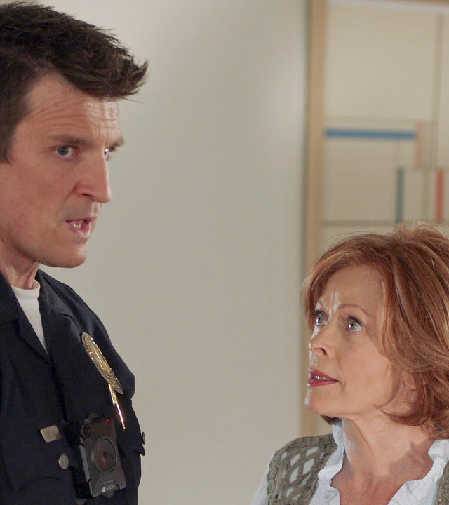 "The Rookie - Familienbande": Nolan (Nathan Fillion) steht Evelyn (Frances Fisher) in einem Gang gegenüber und schaut abgelenkt zur Seite, während Evelyn ihn erwartungsvoll anblickt.