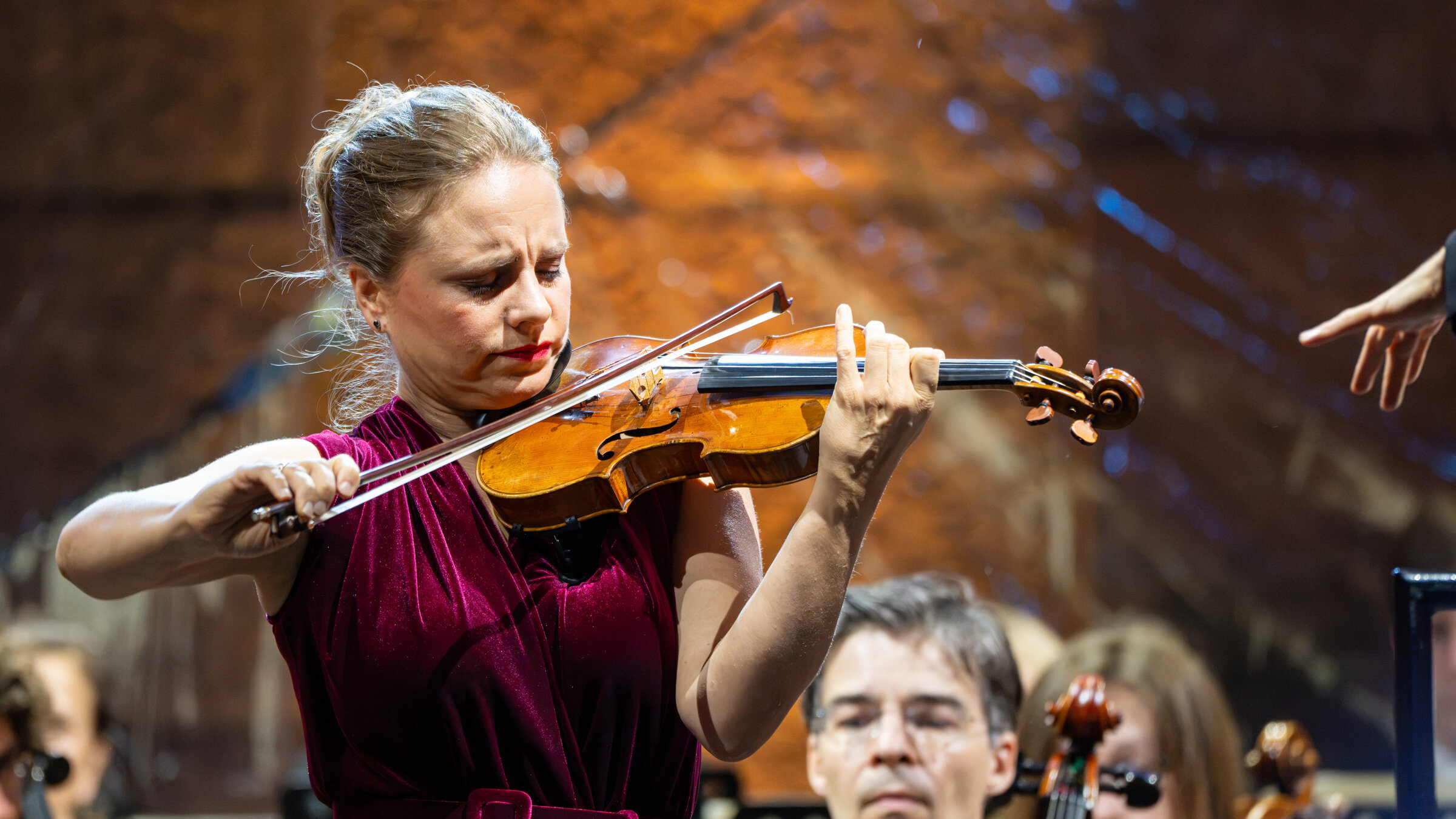 "Julia Fischer auf Schloss Neuschwanstein": Nahaufnahme von Julia Fischer. Sie spielt auf einer Geige. Hinter ihr sind die KÃ¶pfe einiger Orchestermusiker zu sehen.