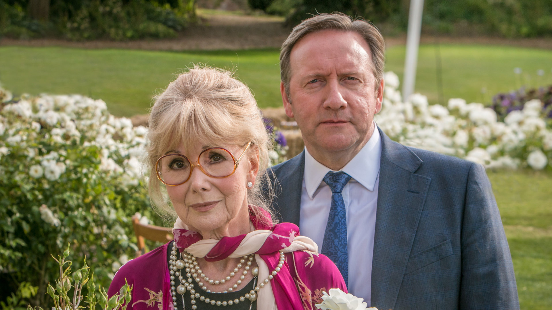 "Inspector Barnaby - Streicheln und töten": John Barnaby (Neil Dudgeon) und Delphi Hartley (Susan Hampshire) stehen auf einer Wiese mit blühenden Blumen und schauen in eine unbestimmte Richtung.