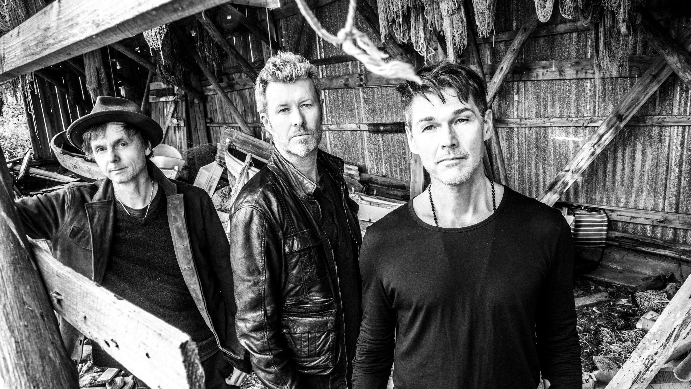 "a-ha:True North": s/w-Foto der Gruppe a-ha. Die drei Bandmitglieder stehen in einem alten Unterstand aus Holz.