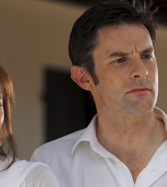 "Death in Paradise - Der blutige Finger": Nahaufnahme Nicole Seymour (Stephanie Beacham) und Alex Seymour (Tom Ward). Beide tragen weiße Oberteile und scheinen jemanden anzusehen.