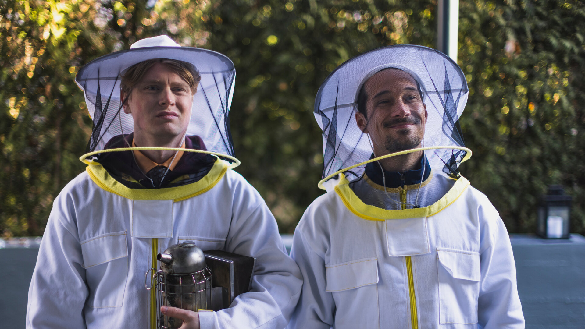 "SPYON - Der erste Außeneinsatz": Asel Asanow (Lukas Zumbrock) und Andreas Rödig (Klaus Steinbacher) stehen im Freien tragen Imkeranzüge. Asel Asanow hält einen Bienen-Smoker in der Hand.