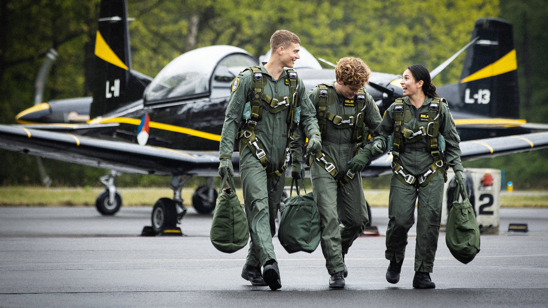 "High-Flyers - Ikarus": Leyla Demir (Sinem Kavus), Guus Walema (Soy Kroon) und Rutger de Man (Josha Stradowski) laufen in ihren Uniformen nebeneinander her. Hinter ihnen steht das Schulungsflugzeug PC-7.