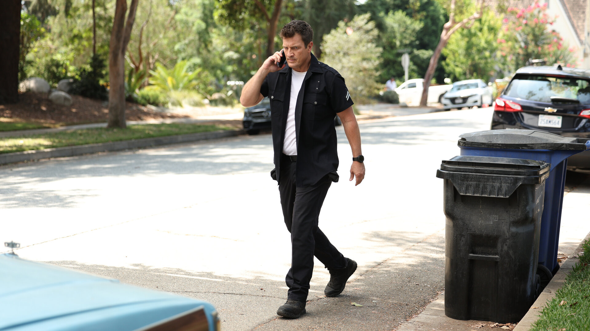 "The Rookie - Die Henkersmahlzeit": Officer John Nolan (Nathan Fillion) läuft telefonierend auf einer unbefahrenen Straße an Mülltonnen vorbei.
