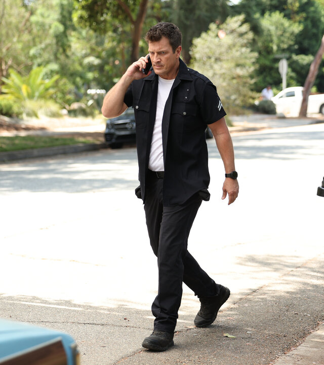 "The Rookie - Die Henkersmahlzeit": Officer John Nolan (Nathan Fillion) läuft telefonierend auf einer unbefahrenen Straße an Mülltonnen vorbei.
