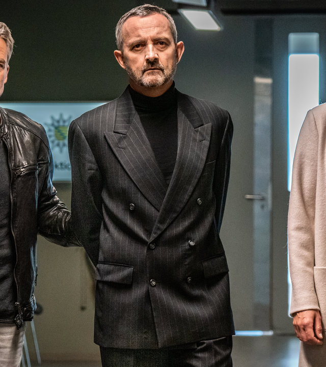 "SOKO Leipzig - Family Business (2)": Jan Maybach (Marco Girnth), Davide Di Maria (Harald Schrott) und Ina Zimmermann (Melanie Marschke) auf dem Gang der Polizeidirektion. Davide hat die Hände auf dem Rücken fixiert und wird von Jan und Ina abgeführt.