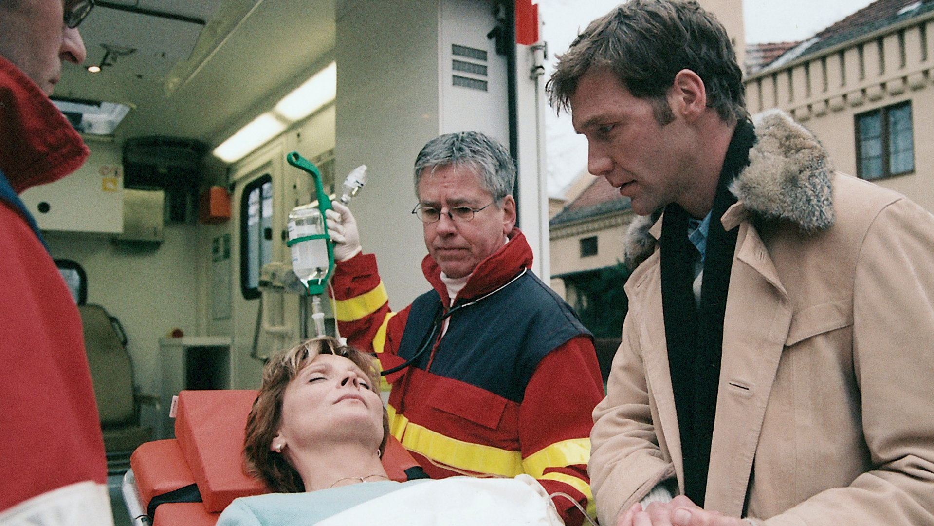 "Bianca - Wege zum Glück: Kapitel 96": Notarzt: Ariane (Kerstin Gähte) liegt bewusstlos auf der Krankenliege. Sie wird von einem Notarztteam versorgt. Oliver (Patrik Fichte) hält ihre Hand und kümmert sich um sie.