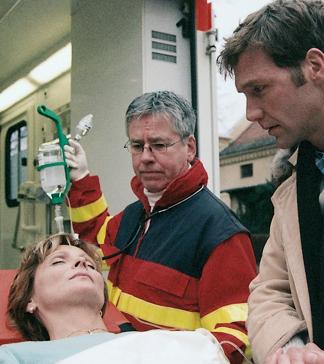 "Bianca - Wege zum Glück: Kapitel 96": Notarzt: Ariane (Kerstin Gähte) liegt bewusstlos auf der Krankenliege. Sie wird von einem Notarztteam versorgt. Oliver (Patrik Fichte) hält ihre Hand und kümmert sich um sie.