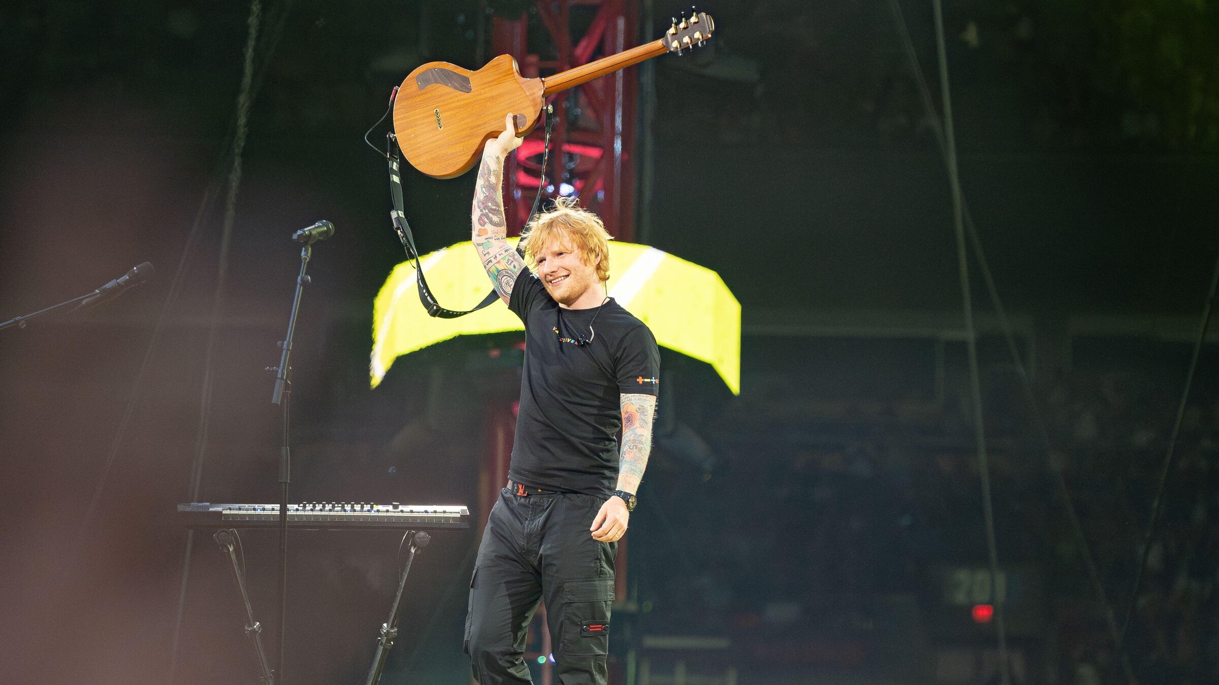 "The True Story of Ed Sheeran": Ed Sheeran hebt lÃ¤chelnd seine Gitarre in die Luft und steht allein auf einer groÃen BÃ¼hne mit Equipment im Hintergrund.