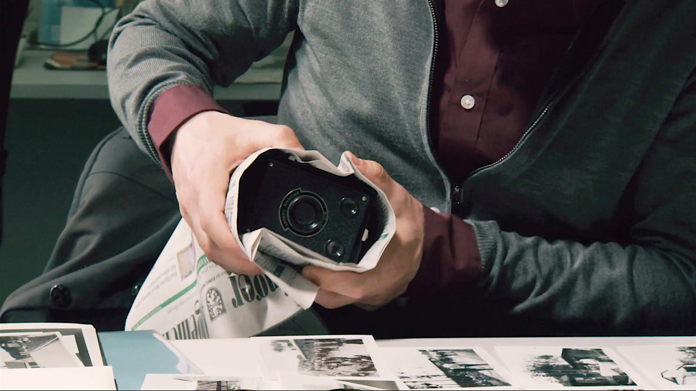 "Blinden Schrittes": Alte Kamera in Zeitungspapier gewickelt in der Armbeuge eines Mannes dessen Gesicht man nicht sieht.