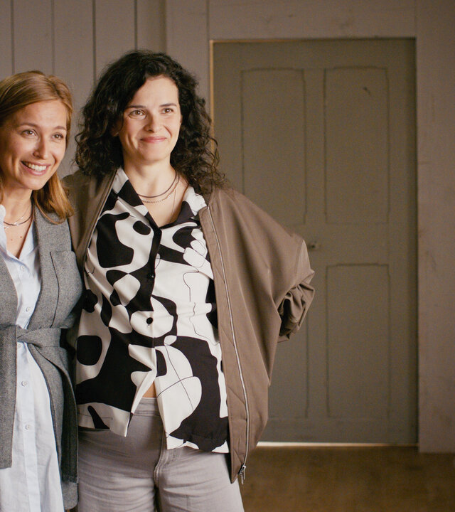 "Lena Lorenz - Kreuz und queer": In der Hebammenpraxis stehen Alex (Pina Kühr) und Franzi Winkler-Ertl (Maxine Kazis) gegenüber von Lena Lorenz (Judith Hoersch), die mit dem Rücken zur Kamera steht. Die beiden Frauen haben die Arme umeinander gelegt und schauen Lena lachend an.