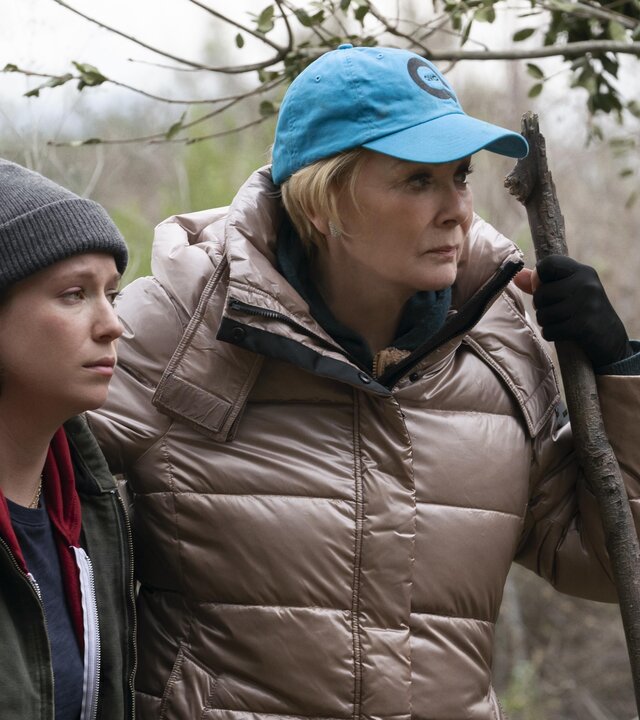 "Hacks - Eines Tages ist jetzt": Deborah und Ava stehen in Outdoorkleidung nebeneinander. Deborah hält in ihrer Hand einen großen Stock, auf den sie sich zu stützt. Um sie herum stehen Bäume und Sträucher.