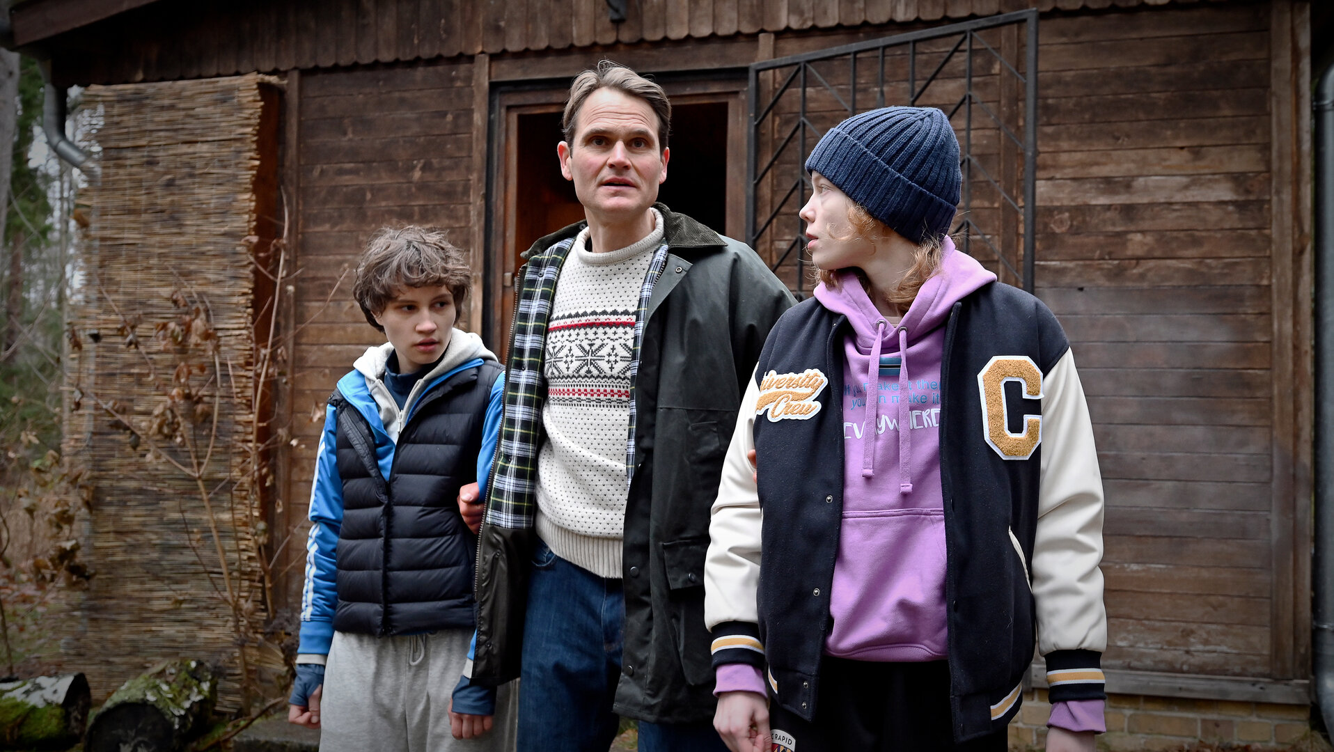 "Jenseits der Spree - Eine muss sterben": Stella (Luna Jordan), Rico Heilmann (Fabian Hinrichs) und Emmi (Bella Bading) stehen nebeneinander vor einer Hütte im Wald. Heilmann hat die beiden fest im Griff.