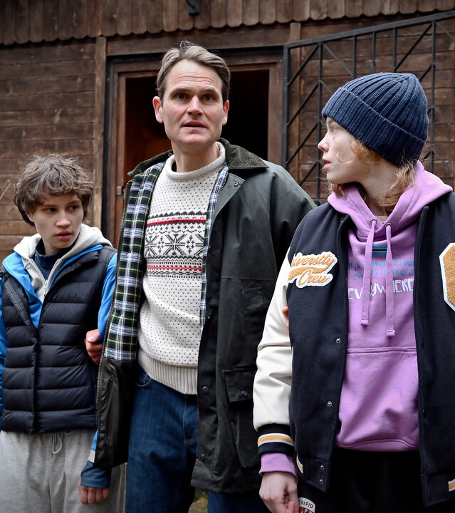 "Jenseits der Spree - Eine muss sterben": Stella (Luna Jordan), Rico Heilmann (Fabian Hinrichs) und Emmi (Bella Bading) stehen nebeneinander vor einer Hütte im Wald. Heilmann hat die beiden fest im Griff.