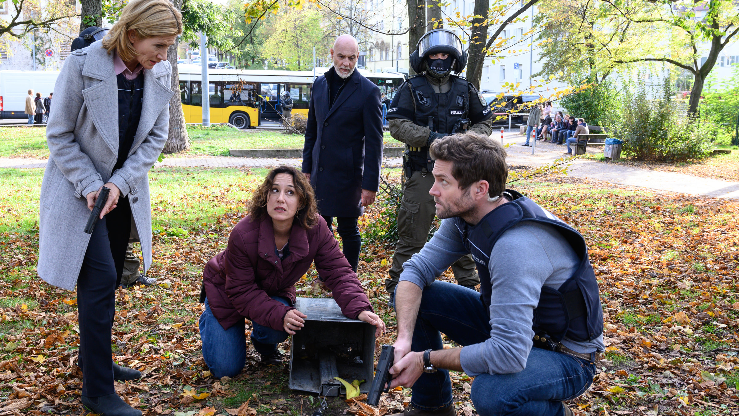 "SOKO Stuttgart - Gift": In einer Grünanlage entdecken Martina Seiffert (Astrid M. Fünderich), Sibylle Beyer (Bärbel Stolz) und Jo Stoll (Peter Ketnath) den leeren Mülleimer, in dem sich zuvor die Tasche mit dem Lösegeld befand. Sibylle kniet auf dem Boden und hält den leeren Mülleimer. Stoll befindet sich neben ihr in der Hocke. Seiffert und Stoll tragen schusssichere Westen und haben ihre Dienstwaffen gezogen. Im Hintergrund beobachten Heiko Biedermann (Simon Licht) und ein vermummter Beamter der Spezialeinheit (Komparse) die Szene.