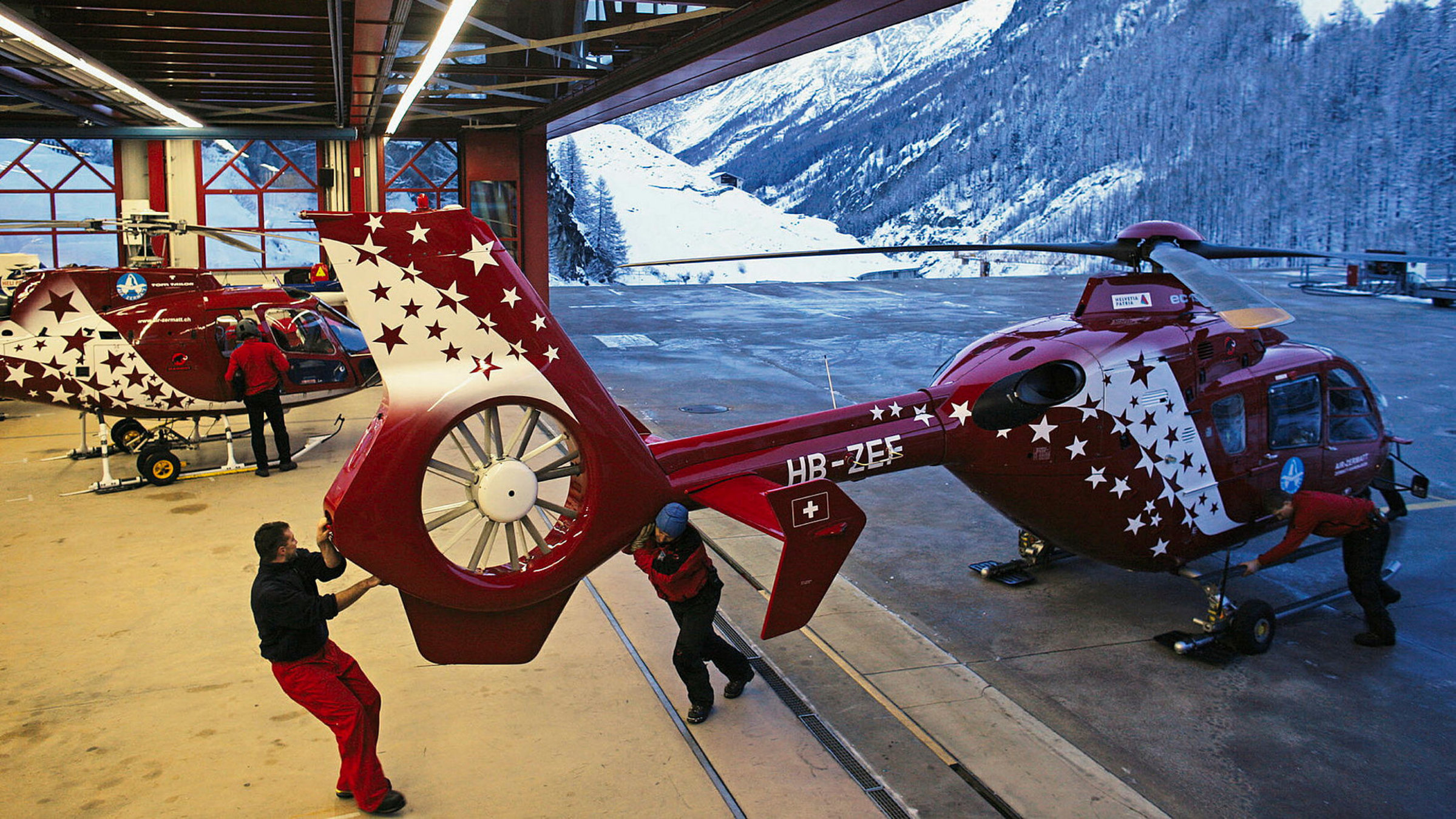 "Die Bergretter - Unterwegs mit der Air Zermatt - Heiratsantrag und Spaltensturz": Abendstimmung auf der Basis - Die Helikopter werden in den Hangar geschoben.