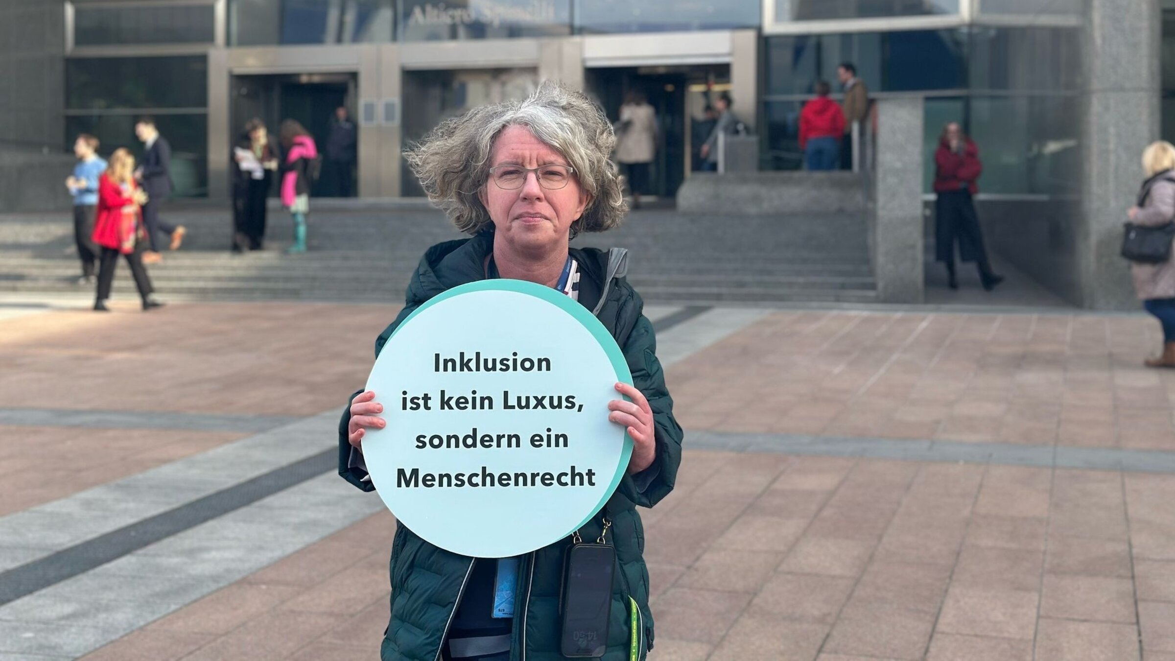 "Einfach Mensch: Stimmen für die Inklusion": Katrin Langensiepen steht vor dem EU-Parlament in Brüssel. Sie hält ein Schild mit der Aufschrift "Inklusion ist kein Luxus, sondern ein Menschenrecht".