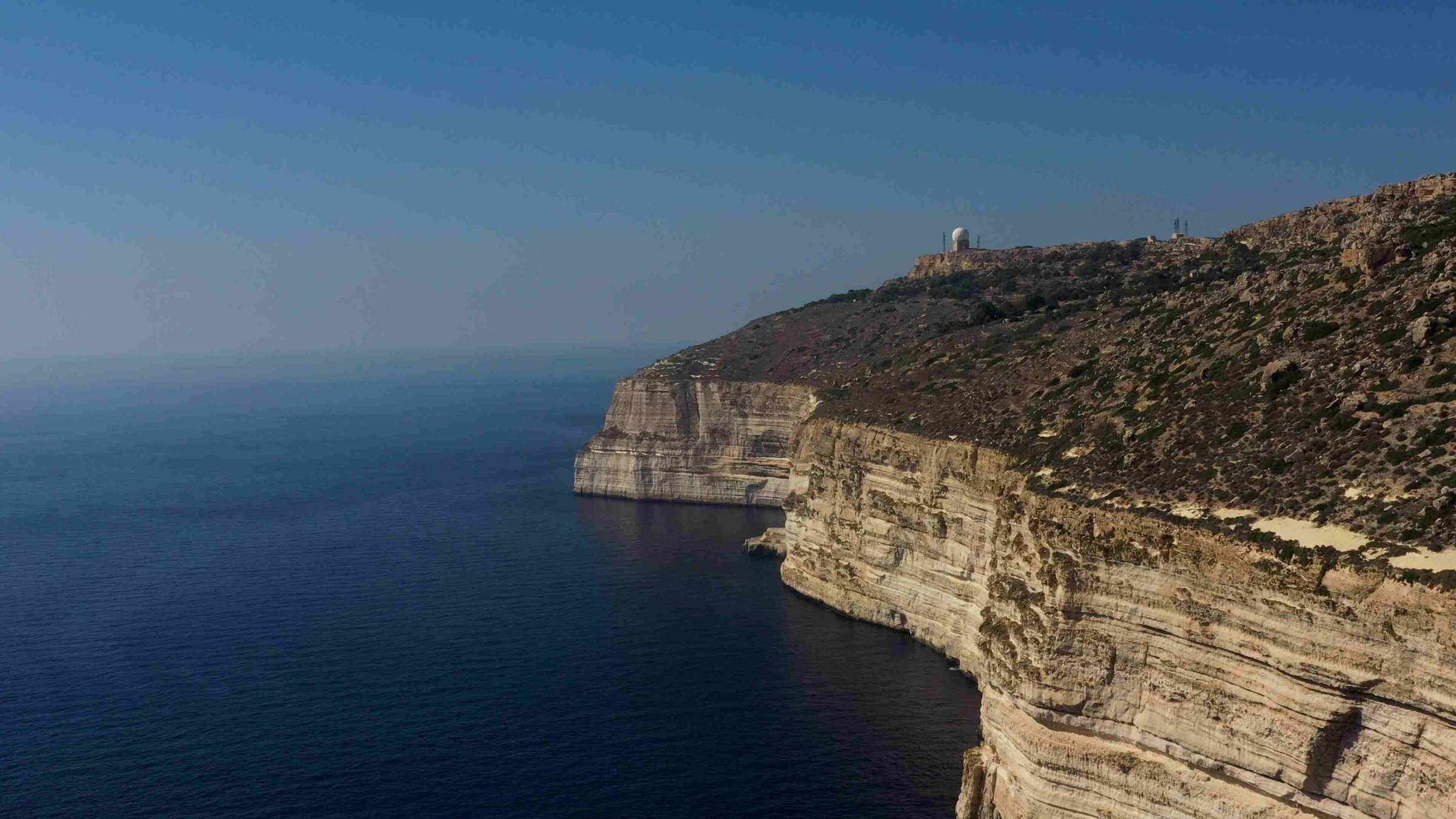 "Traumorte - Malta": Luftaufnahme einer Klippe, die steil ins tiefblaue Meer abfällt.