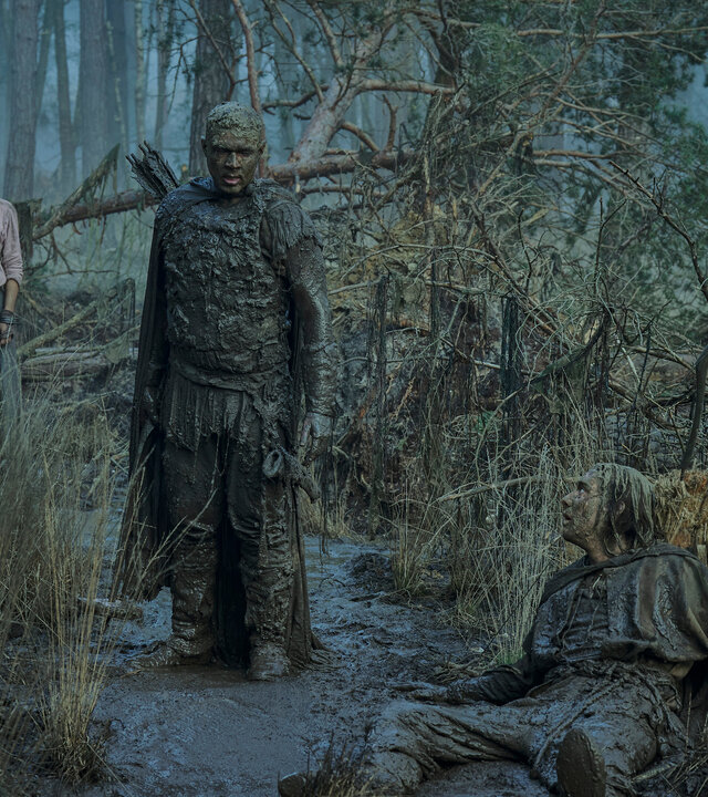 "Der Herr der Ringe: Die Ringe der Macht - Der Älteste": Isildur (Maxim Baldry) liegt in einem Moor. Arondir (Ismael Cruz Córdova) steht daneben. Beide sind von Kopf bis Fuß mit Schlamm bedeckt. Aus dem Hintergrund beobachtet die unversehrte Estrid (Nia Towle) das Geschehen. Sie trägt Handfesseln.