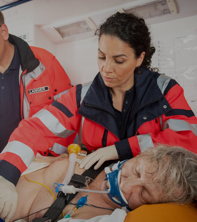 "Notruf Hafenkante - Achtung, Wolf!": Die Notärztin Dr. Sam Jordan (Hanife Sylejmani) und ein Rettungsassistenz (Komparse) stehen in einem Notarztwagen neben einer Patiententrage auf der Haller (Hannes Hellmann) liegt. Er ist auf die linke Seite gedreht und intubiert. Beide sind dabei Haller weiter zu versorgen.