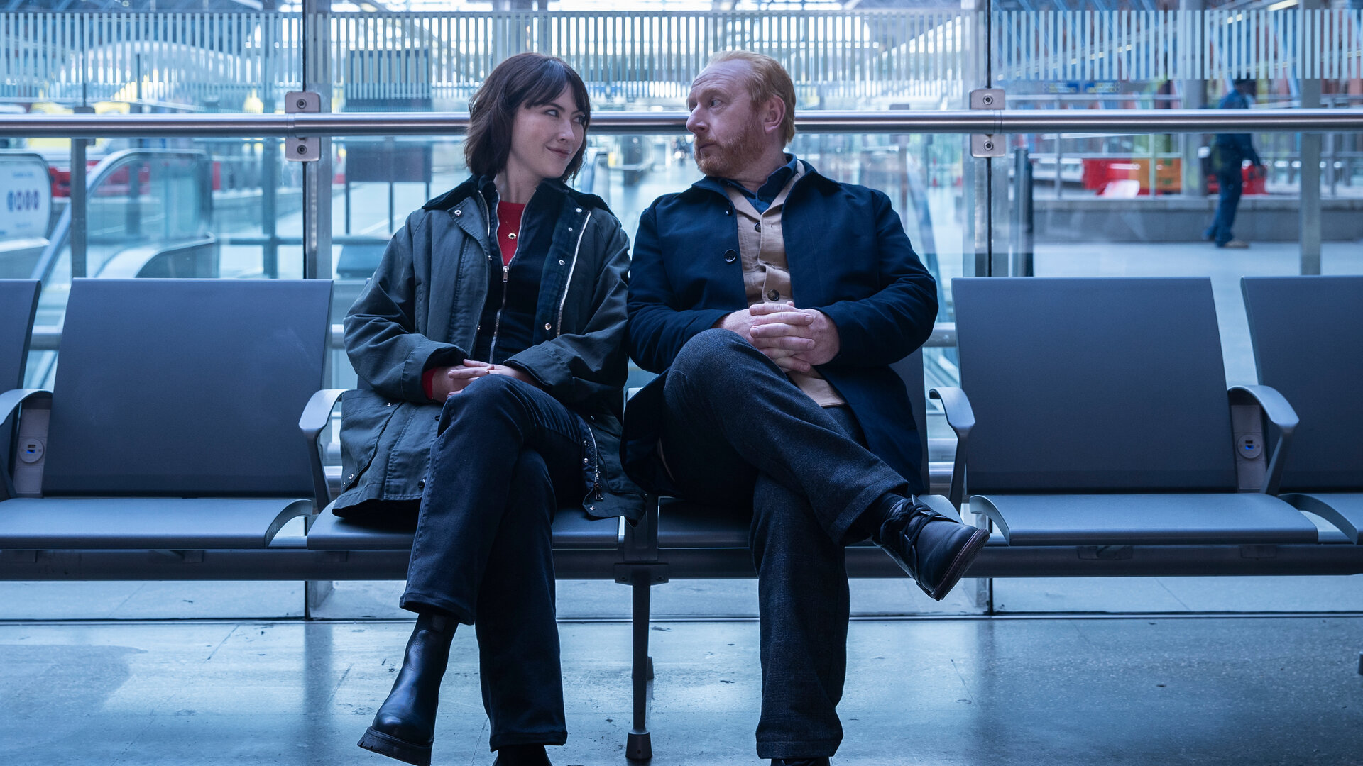 "The Chelsea Detective - Im blauen Zimmer": DS Layla Walsh (Vanessa Emme) und DI Max Arnold (Adrian Scarborough) sitzen nebeneinander auf einer Bank im Londoner Bahnhof St Pancras.