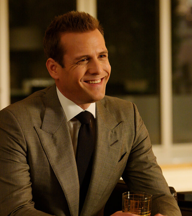 "Suits - Kairo": Harvey (Gabriel Macht) sitzt mit einem strahlenden Lächeln in einem Innenraum in einem Sessel und hält ein Glas in seinen Händen.
