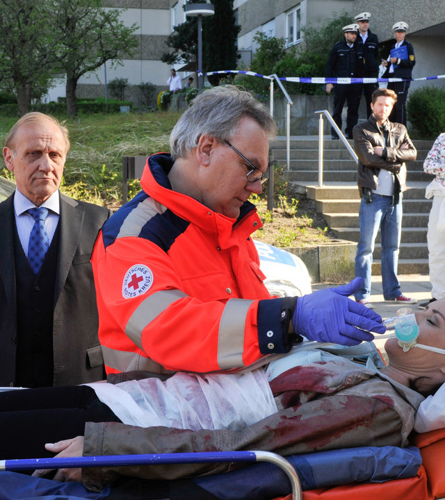 "SOKO Stuttgart - Das Gesetz der Straße": Selma Kirsch (Yve Burbach) ist mit einem Messerstich in die Herzgegend schwer verletzt worden. Sie liegt auf der Trage, neben ihr steht der Notarzt (Komparse). Martina Seiffert (Astrid M. Fünderich) und Michael Kaiser (Karl Kranzkowski) stehen tief bestürzt daneben. Etwas weiter weg stehen genauso entsetzt Jo Stoll (Peter Ketnath) und Jan Arnaud (Mike Zaka Sommerfeldt).
