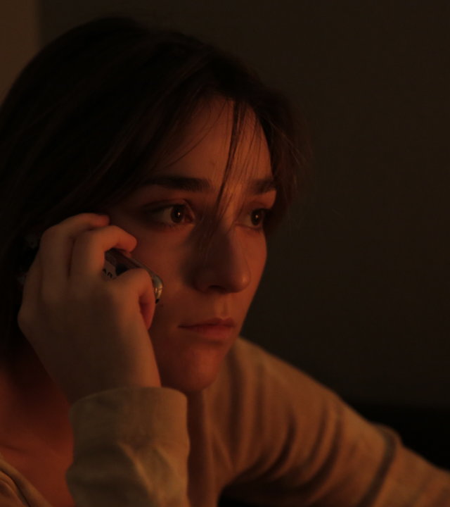 "About Saturday - Gelbes Sofa": Klara (Darin Hagi) sitzt in einer dunklen Ecke und telefoniert mit ihrem Handy.