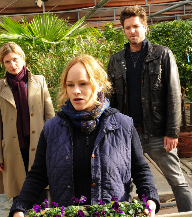 "SOKO Stuttgart - Mord unter Freunden": Martina Seiffert (Astrid M. Fünderich) und Jo Stoll (Peter Ketnath) stehen hinter Franziska Wenzel (Dorkas Kiefer). Diese hält einen Blumenkasten in der Hand. Im Hintergrund stehen mehrere Pflanzen in Töpfen.