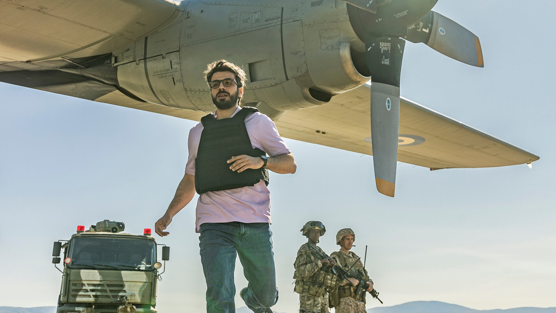 "Kabul - Flucht aus der Hölle: Verhandlungssache": Giovanni (Gianmarco Saurino) befindet sich am Flughafen von Kabul. Er läuft nahe an einem startbereiten Transportflugzeug vorbei, während schwer bewaffnete Soldaten im Hintergrund die Stellung halten. Die Atmosphäre ist angespannt und bedrohlich.