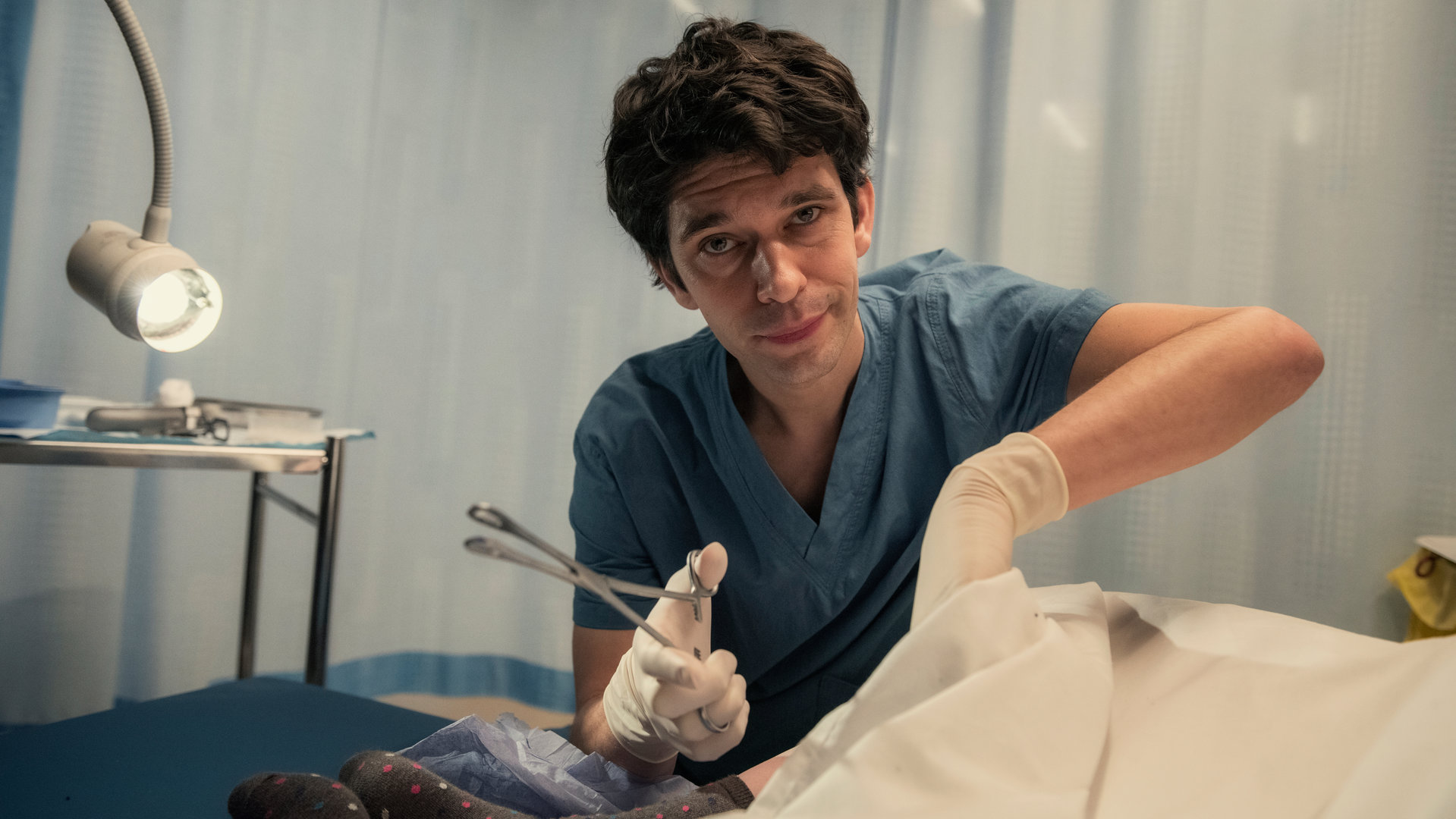 "This Is Going To Hurt - Mal verliert man, mal gewinnen die anderen": Adam (Ben Whishaw) sitzt neben einem Krankenbett und steckt seine Hand unter ein Laken.