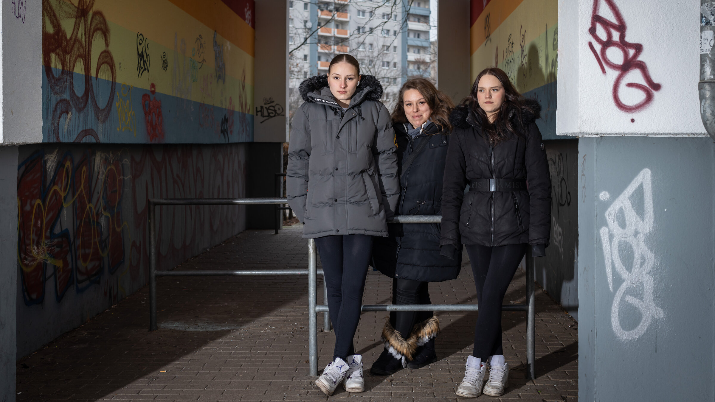 "37 Grad: Vererbte Armut - Kindheit mit wenig Geld": Angie (18), Luisa (16) und ihre Mutter Silvana (36) stehen an Stangen gelehnt in einem Hausdurchgang. In dem Gang befinden sich Graffitis, dahinter steht ein Hochhaus.