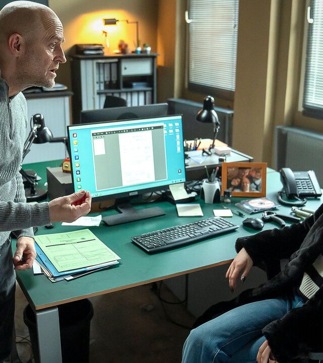 "Jenseits der Spree - Carlotta": Im Büro: Robert (Jürgen Vogel) redet eindringlich mit Carlotta (Lea Zoë Voss) die an einem Schreibtisch sitzt. Er steht dabei vor ihr und gestikuliert mit der Hand, während Carlotta ihn fragend anschaut.