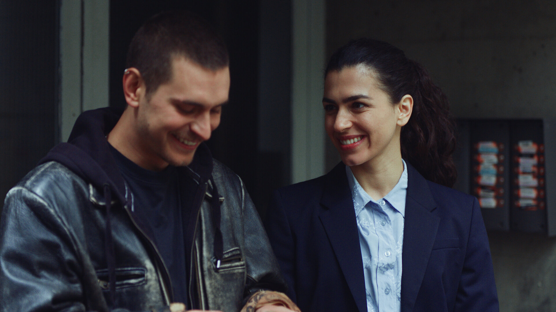 "Crystal Wall - Opfer": Louna Lloris (Anna Bardavelidze) und Liam (Ludwig Brix) stehen nebeneinander im Hauseingang und lachen gemeinsam.