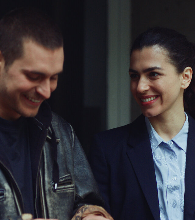 "Crystal Wall - Opfer": Louna Lloris (Anna Bardavelidze) und Liam (Ludwig Brix) stehen nebeneinander im Hauseingang und lachen gemeinsam.