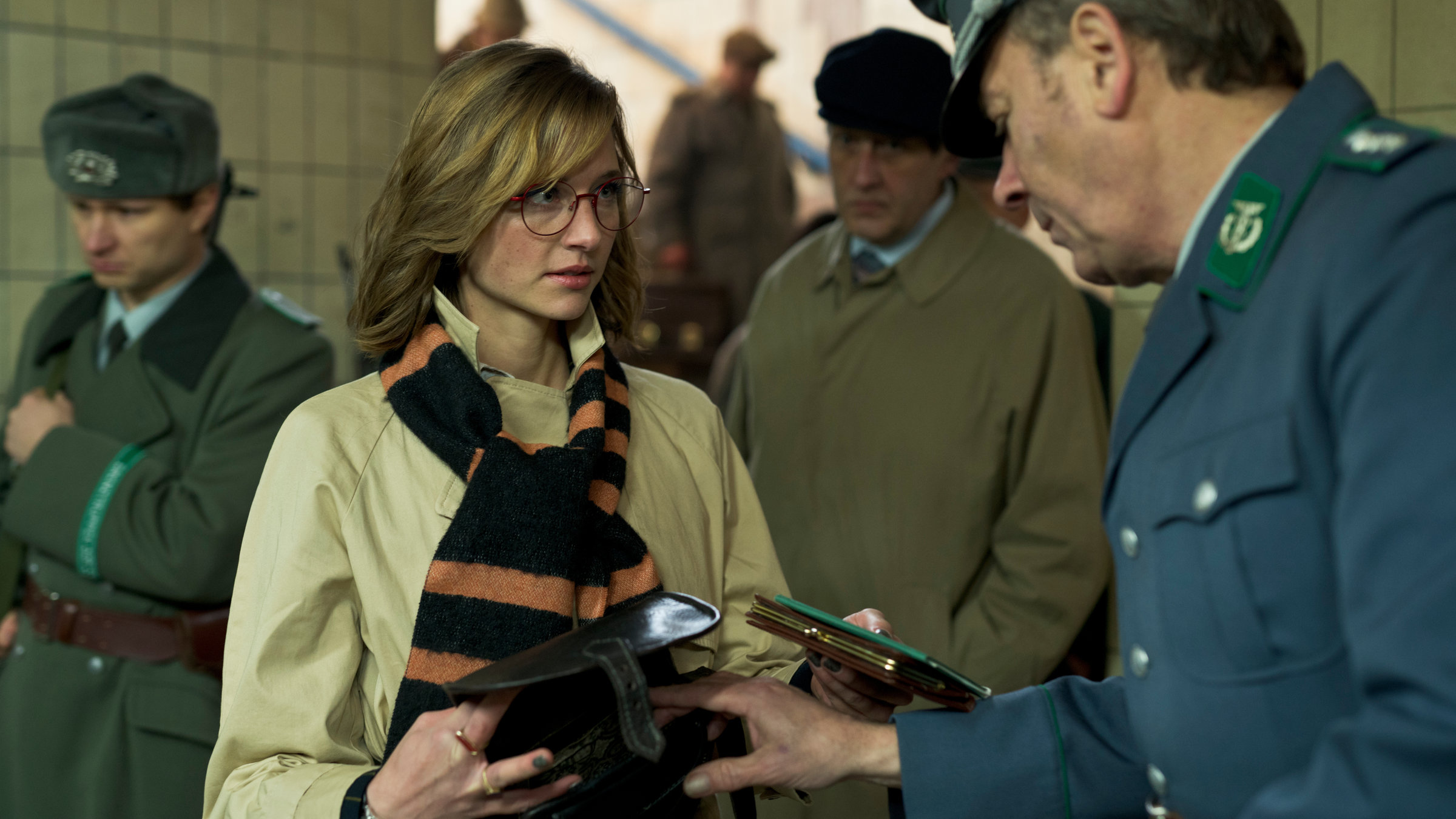 "Der Palast (2)": Chris (Svenja Jung) gibt einem Kontrolleur an der Grenze zum Westen ihren Pass. Der Mann wirft dabei einen Blick in ihre geöffnete Handtasche.