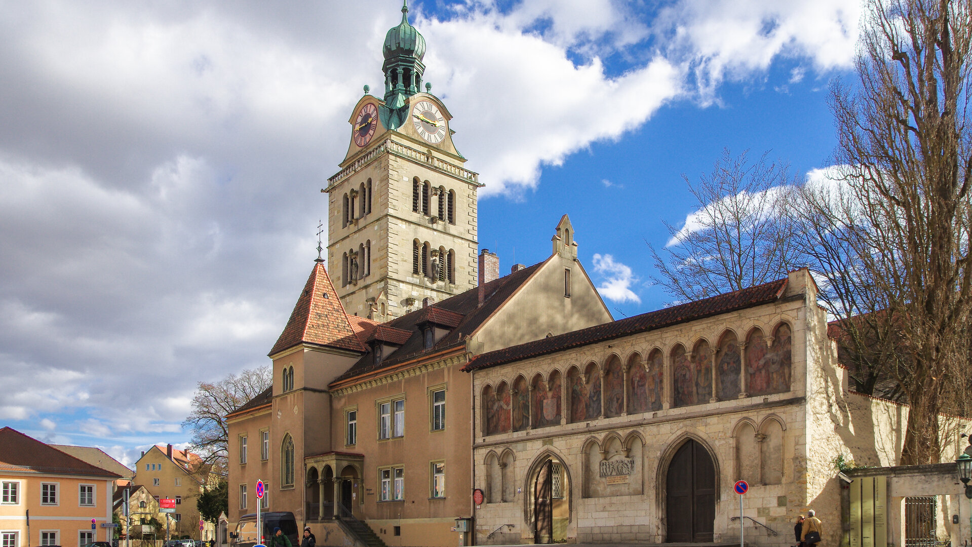 "Katholischer Gottesdienst - Lernen, Mensch zu sein": Blick auf den Kirchturm der Basilika St. Emmeram in Regensburg und das Emmeram Forum.