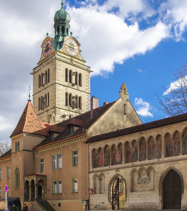 "Katholischer Gottesdienst - Lernen, Mensch zu sein": Blick auf den Kirchturm der Basilika St. Emmeram in Regensburg und das Emmeram Forum.