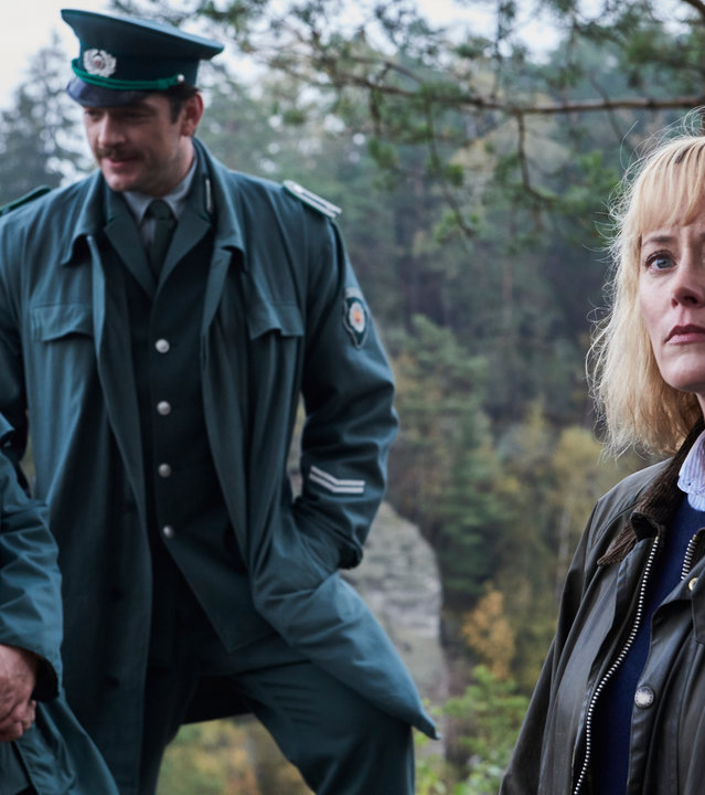 „Walpurgisnacht - Die Mädchen und der Tod (1)“: Lothar Wieditz (Jörg Schüttauf) und Karl Albers (Ronald Zehrfeld), die beide eine grüne Polizeiuniform tragen, stehen nebeneinander im Freien und schauen sich an. Leicht versetzt vor ihnen steht Nadja Paulitz (Silke Bodenbender). Im Hintergrund sind Bäume zu erkennen.