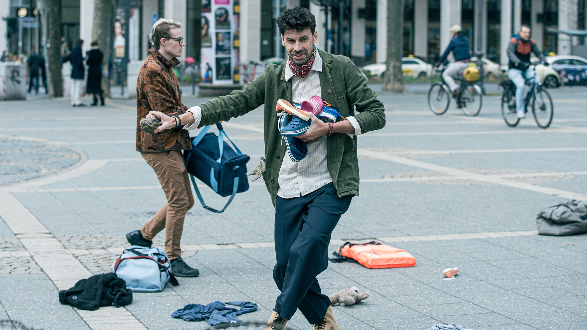 "Ein Fall für zwei - Ausgetanzt": Tagsüber eilt Amadeo Reyes (Juan Lo Sasso), ein Mann mittleren Alters mit dunklem Haar, über einen städtischen Platz . Er trägt einige bunte Gartenschuhe vor der Brust. Um ihn herum herrscht geschäftiges Treiben: Menschen mit Taschen laufen vorbei, zwei Radfahrer fahren in entgegengesetzte Richtungen und verstreute Kleidungsstücke und Taschen liegen auf dem gepflasterten Boden.