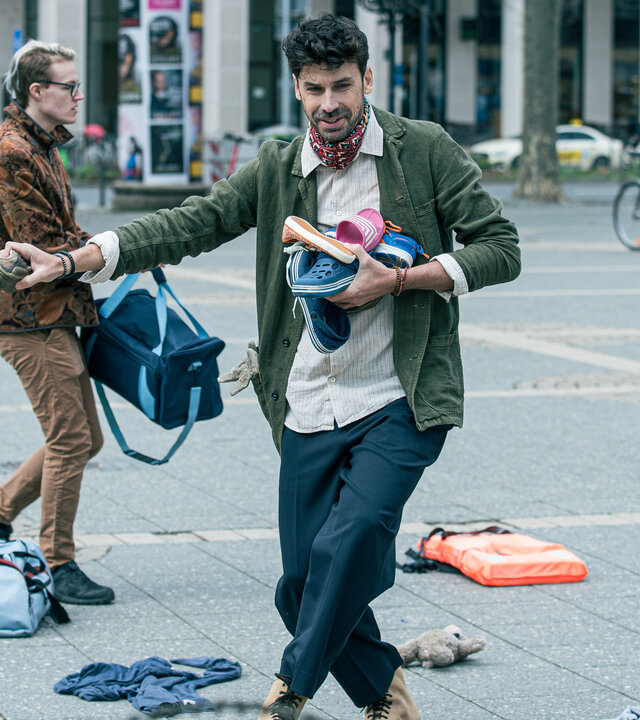 "Ein Fall für zwei - Ausgetanzt": Tagsüber eilt Amadeo Reyes (Juan Lo Sasso), ein Mann mittleren Alters mit dunklem Haar, über einen städtischen Platz . Er trägt einige bunte Gartenschuhe vor der Brust. Um ihn herum herrscht geschäftiges Treiben: Menschen mit Taschen laufen vorbei, zwei Radfahrer fahren in entgegengesetzte Richtungen und verstreute Kleidungsstücke und Taschen liegen auf dem gepflasterten Boden.