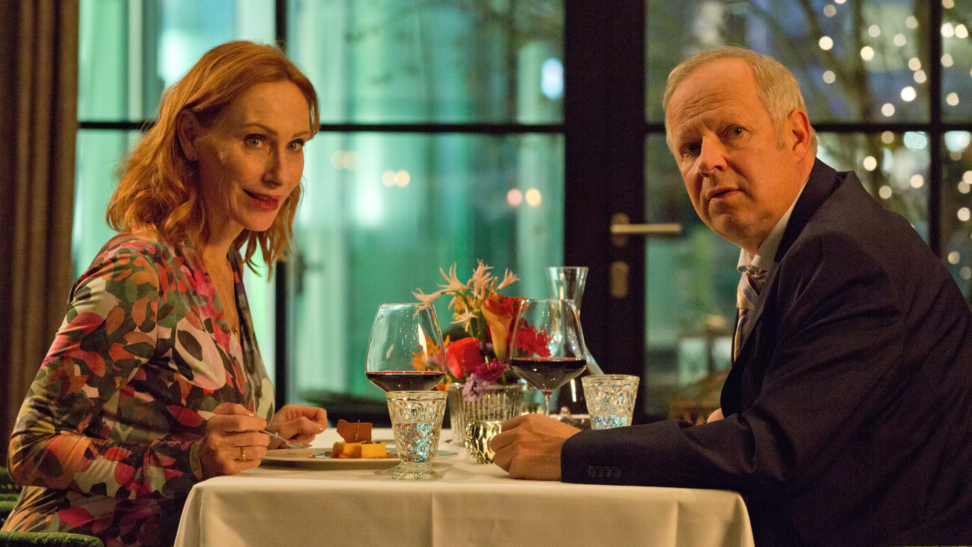 "Familie Bundschuh - Wir machen Abitur": Gundula (Andrea Sawatzki) und Gerald (Axel Milberg) sitzen in einem Restaurant am Tisch und schauen in die Kamera.