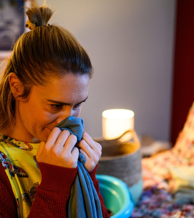 "Bettys Diagnose - Sprachlos": Betty (Henrike Hahn) sitzt auf ihrem Bett und riecht an einem blauen Pullover, den sie in den Händen hält.