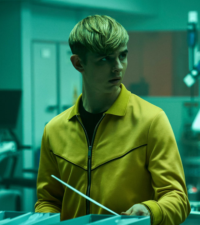 "Alex Rider - Verschwörung": Alex Rider (Otto Farrant) steht in einem grün beleuchteten Raum. Vor ihm steht eine Reihe von Ordnern. Alex blickt schockiert zur Seite.